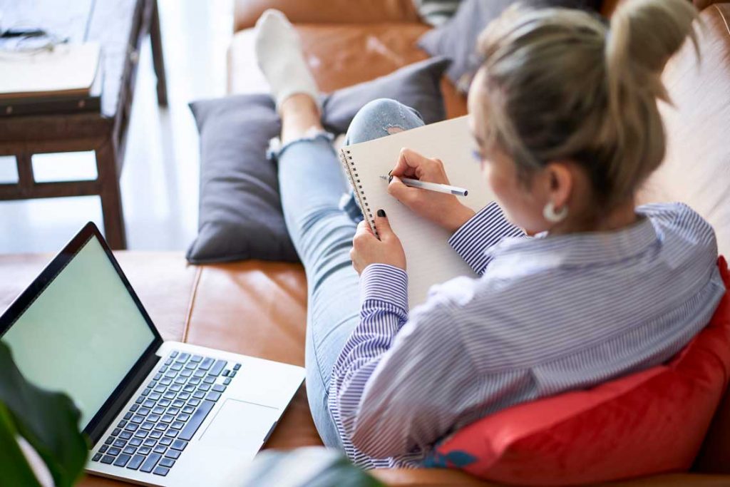 woman on couch with notebook and laptop