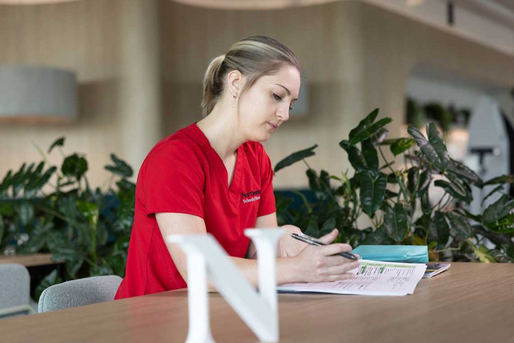 NEU nursing student at desk writing notes
